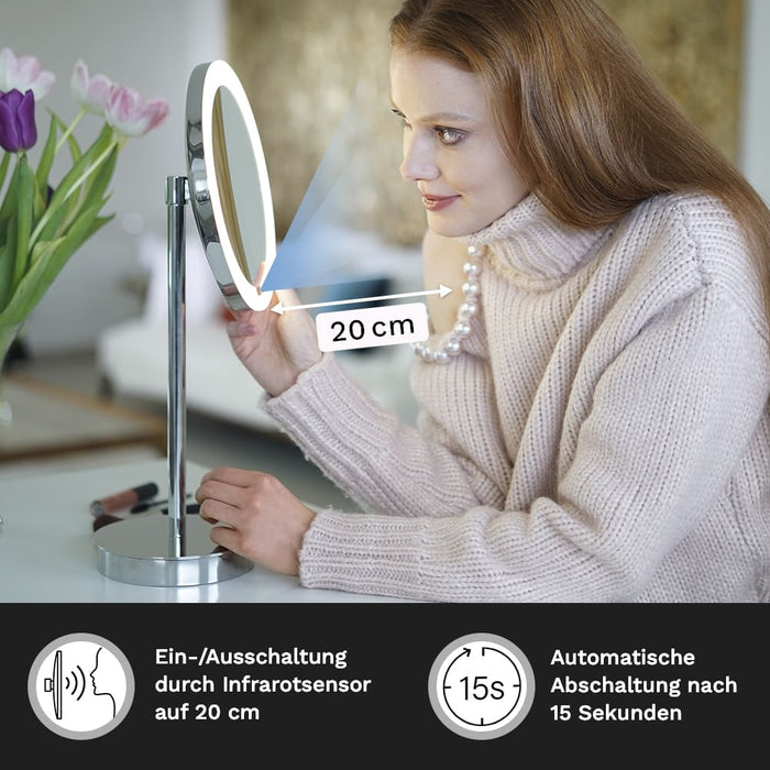Eine Frau betrachtet sich im LED Interface Kosmetikspiegel von Aliseo, Der Standspiegel hat ein modernes Design, Rundes Spiegelglas mit Ambiente-Hintergrundbeleuchtung, integriertem Infrarotsensor schaltet das Licht automatisch ein und aus