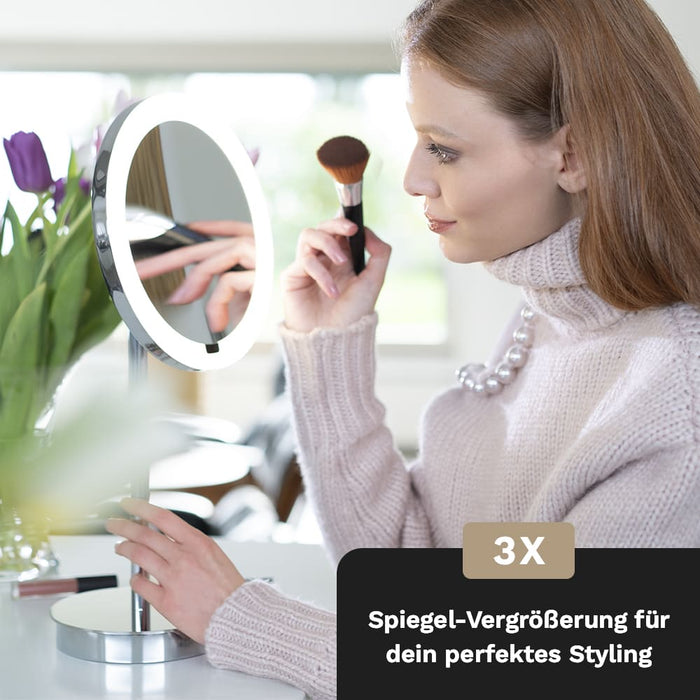 Eine Frau betrachtet sich im LED Interface Kosmetikspiegel von Aliseo. Der Standspiegel hat ein modernes Design, Rundes Spiegelglas mit Ambiente-Hintergrundbeleuchtung und eine 3x Vergrößerung für das perfekte Styling