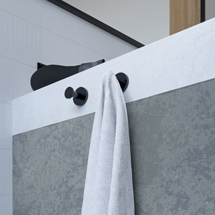 Zwei runde Nexxus Haken in Schwarz matt sind an einem Badschrank montiert. Ein Handtuch hängt an einem Haken. Helles, weißes Badezimmer.