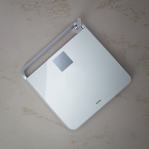 Nevis Personenwaage  – flaches, modernes Design in Silber hängt an einem Haken an einer Betonwand.